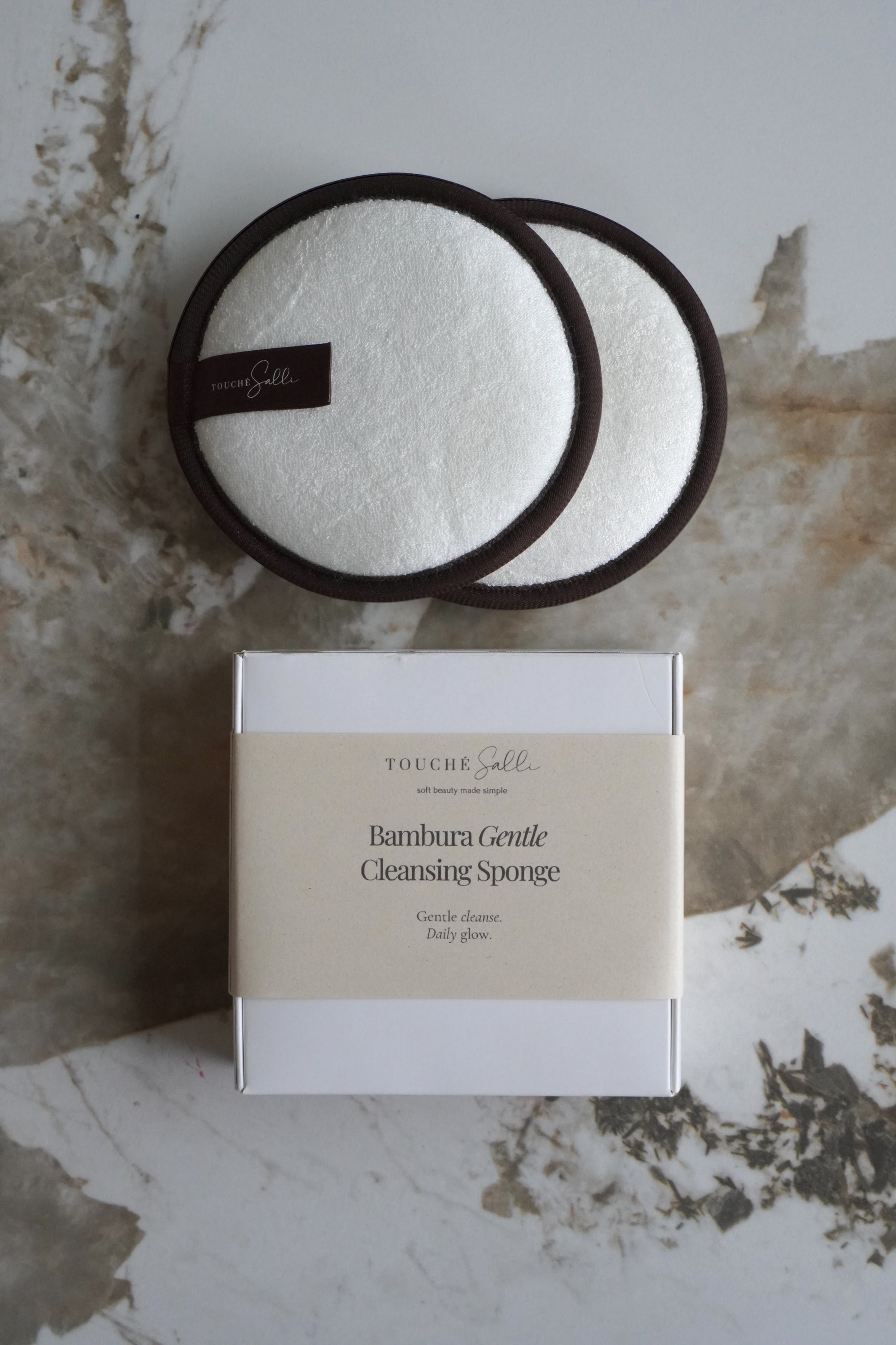 Touché Salli Bambura Gentle Cleansing Sponge, 2 stk. Hvide bambusfrotté svampe med mørkebrune kanter.