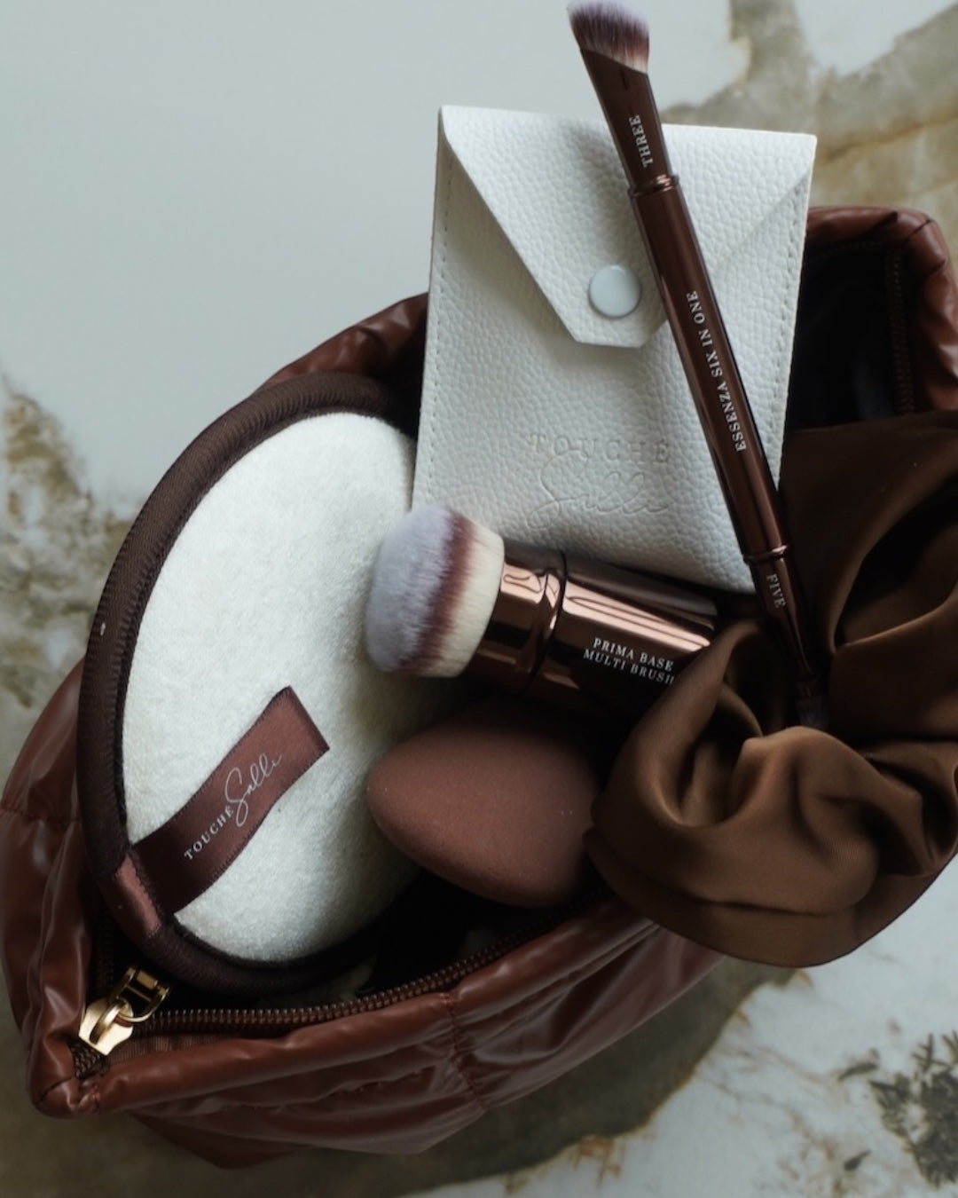 Touché Salli Espresso Quilted Case kosmetiktaske i mørkebrun med quiltet struktur, indeholder makeup-børster og svampe.